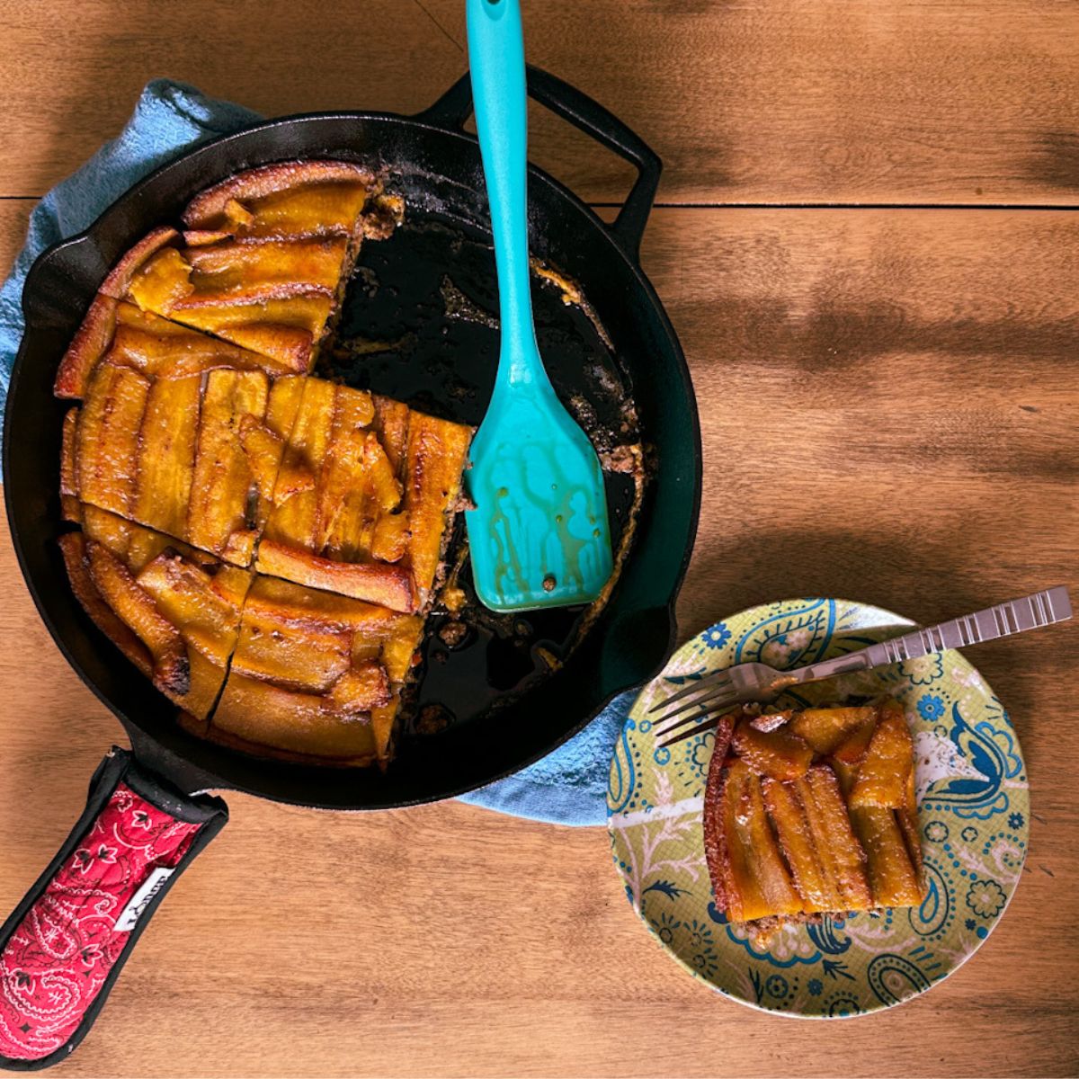 Pastelon in a cast iron skillet with a slice served on a green plate.