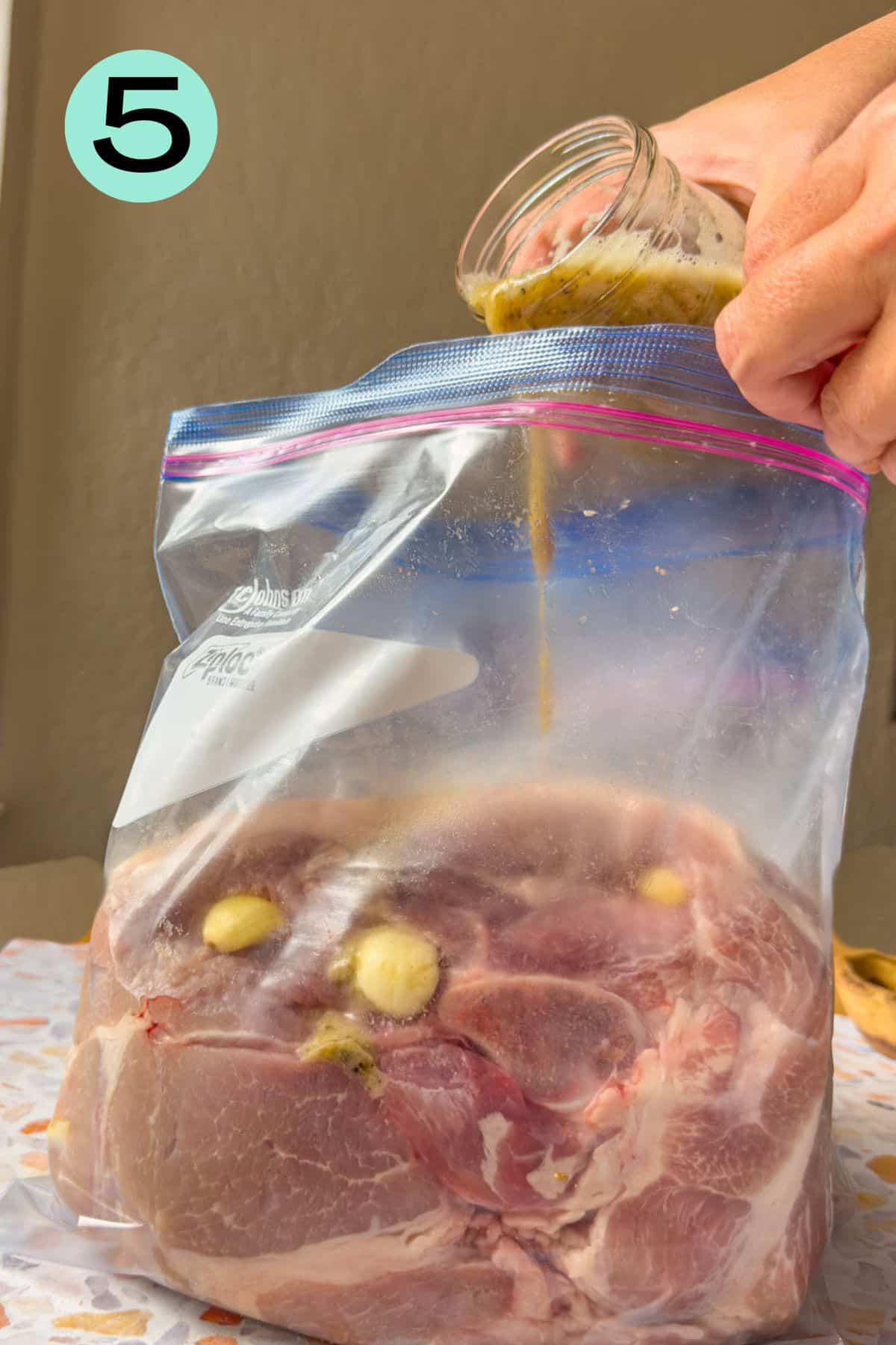The ziplock bag with the cut of pork is on the table and mojo marinade is being poured into the bag.