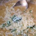 Close up of roasted vegetable bisque in a bowl with shredded asiago cheese and culantro chiffonade