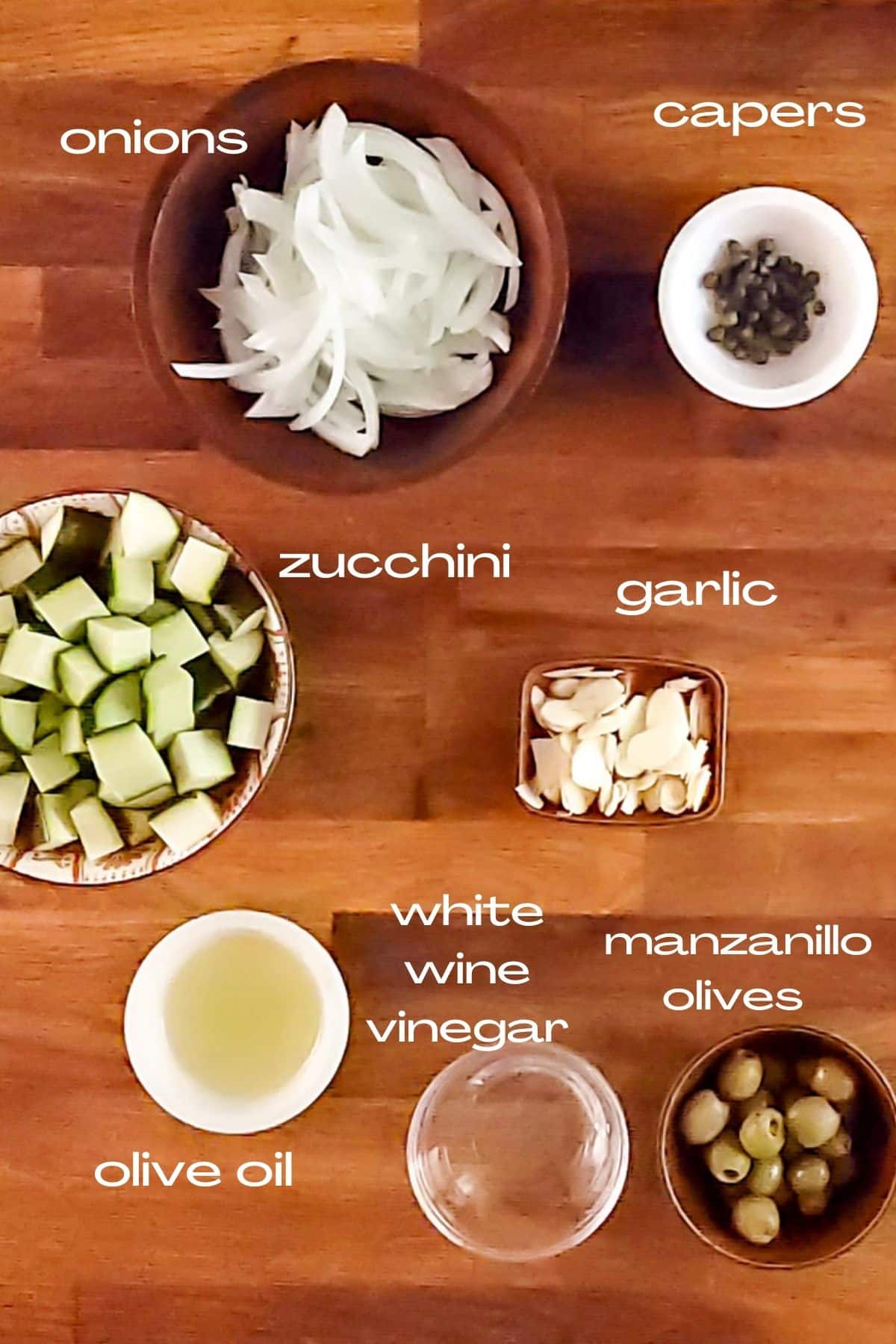 ingredients for zucchini en escabeche; zucchini, onions, garlic, Spanish olives, capers, olive oil, and white wine vinegar.