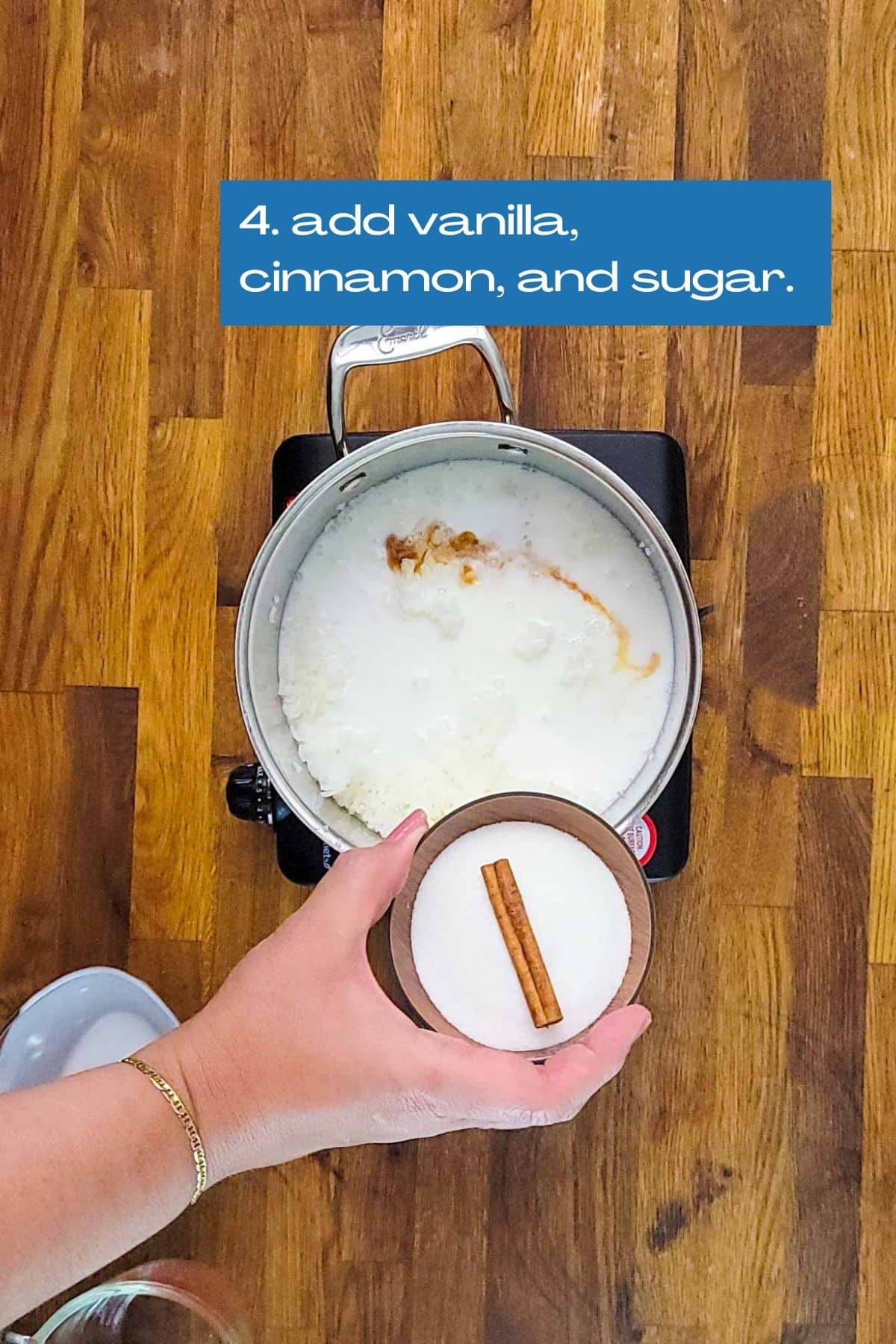 A sauce pan with rice, milk, coconut milk, vanilla. Now adding a cup of half a cup of granulated sugar and a cinnamon stick.