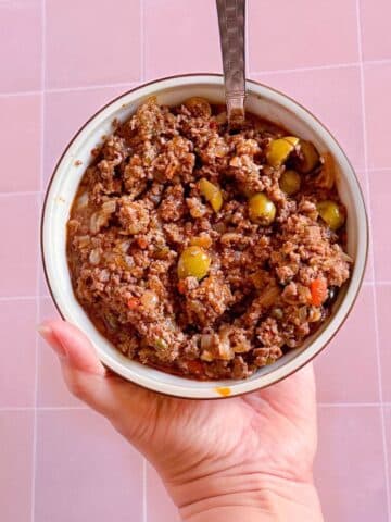 A bowl of picadillo with pieces of green olives, onions, capers, and pimentos mixed throughout.