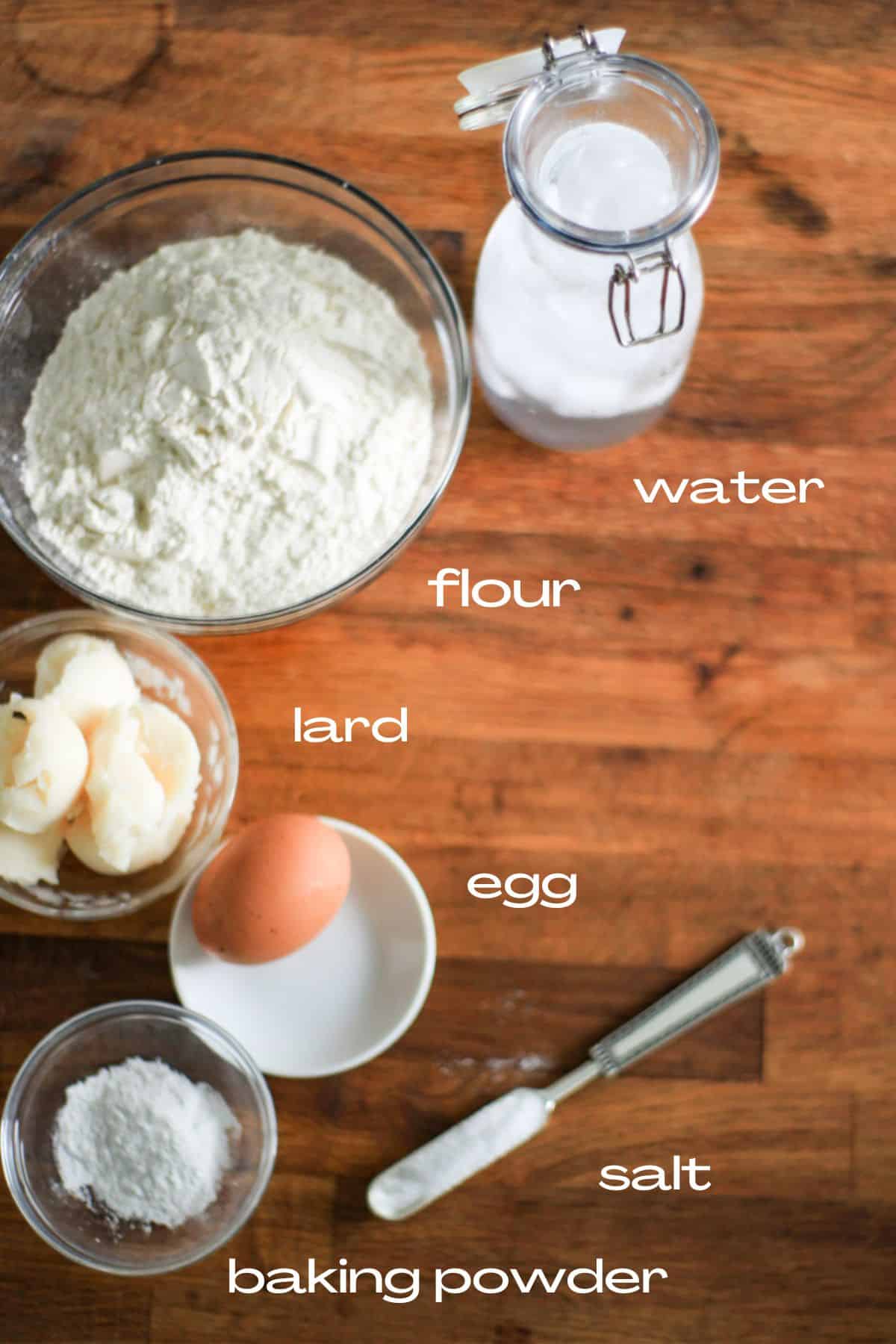 ingredients to make empanada dough. Flour, iced water, fat or lard, egg, baking powder, and salt
