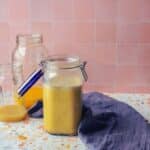 mason jar filled with freshly made mojo. There is a blue kitchen towel on the right and leftover lime and lemon juice behind the jar of mojo.
