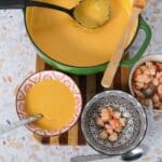 Dutch oven with butternut squash bisque, next to it three bowls. One with bisque, the second with just cooked shrimp waiting to add bisque to it, and the third has the remaining cooked shrimp that will be used as a garnish.