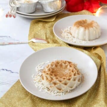 Two small plates with individual tembleques dusted with cinnamon and toasted coconut garnishes. Plates sit over a golden glitter fabric.