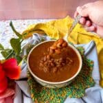 A serving bowl of beans with a spoonful of beans hoving over it.