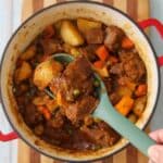 A pot with carne guisada and a large spoon hovering over the pot full of stew.