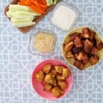 Table with two bowls of meatballs, dipping sauces, and veggies. On the bottom center, a bowl with buffalo chicken meatballs, next to it to the right another bowl with the meatballs that have been fried.