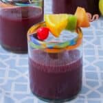 One highball glass of sangria decorated with a fruit skewer of maraschino cherries, oranges, kiwi, and plums.