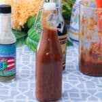 A bottle of mojito sauce surrounded by a bottle of pique (hot sauce), Worcestershire sauce, and the remaining sauce.