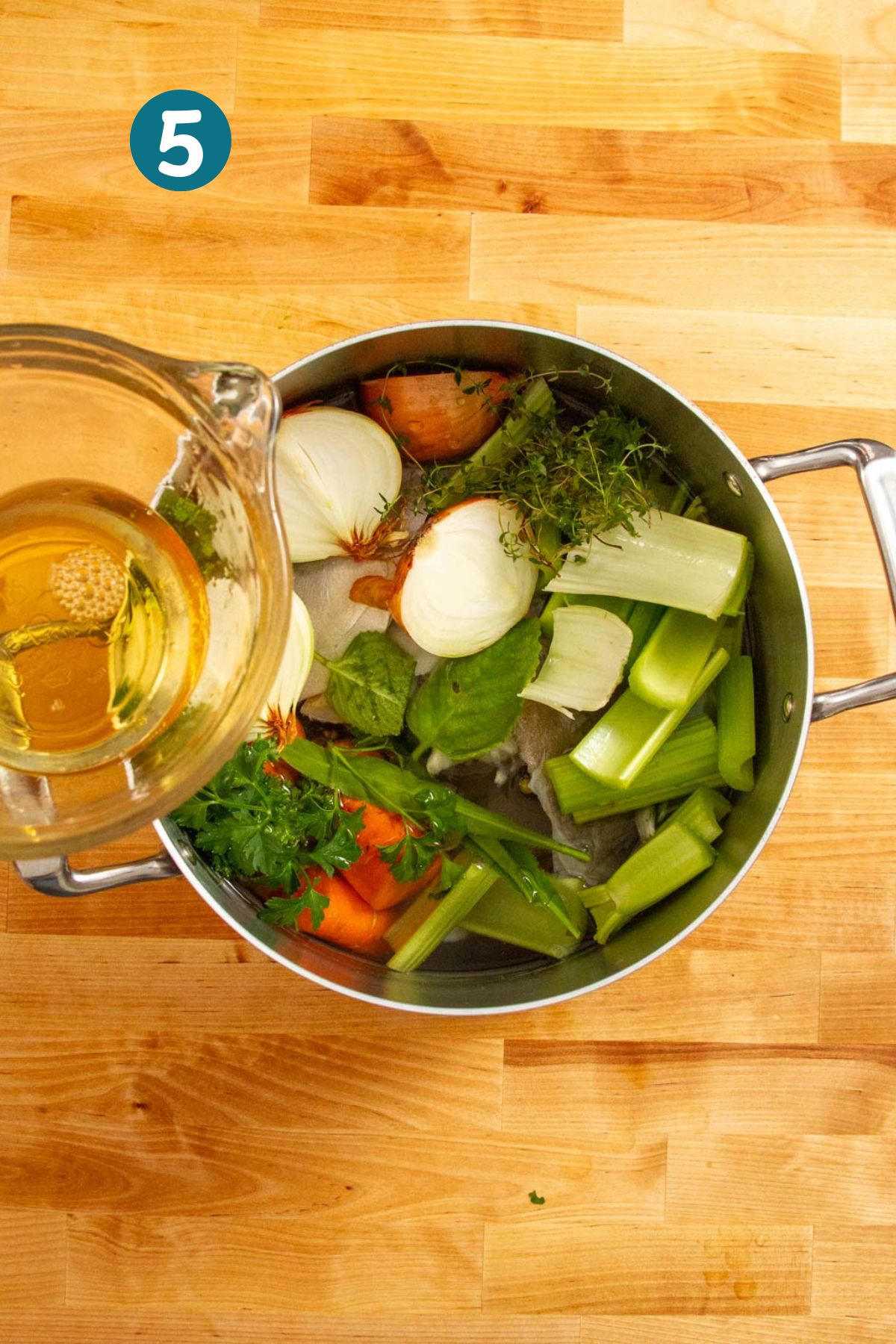 Pouring water into the pot over fish, vegetables, and herbs to begin simmering the broth.