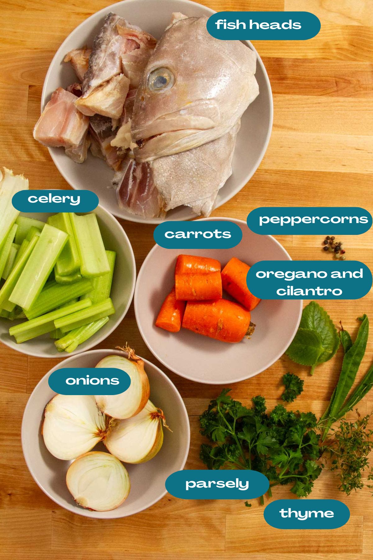 Overhead view of labeled ingredients for Puerto Rican fish broth, including fish heads, onions, celery, carrots, herbs, and peppercorns.