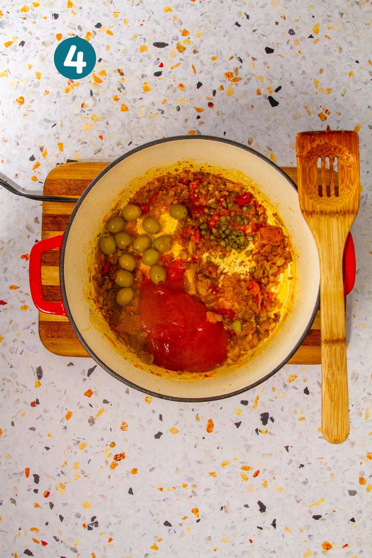 Green olives, capers, and tomato sauce are being added to the mixture in the Dutch oven.