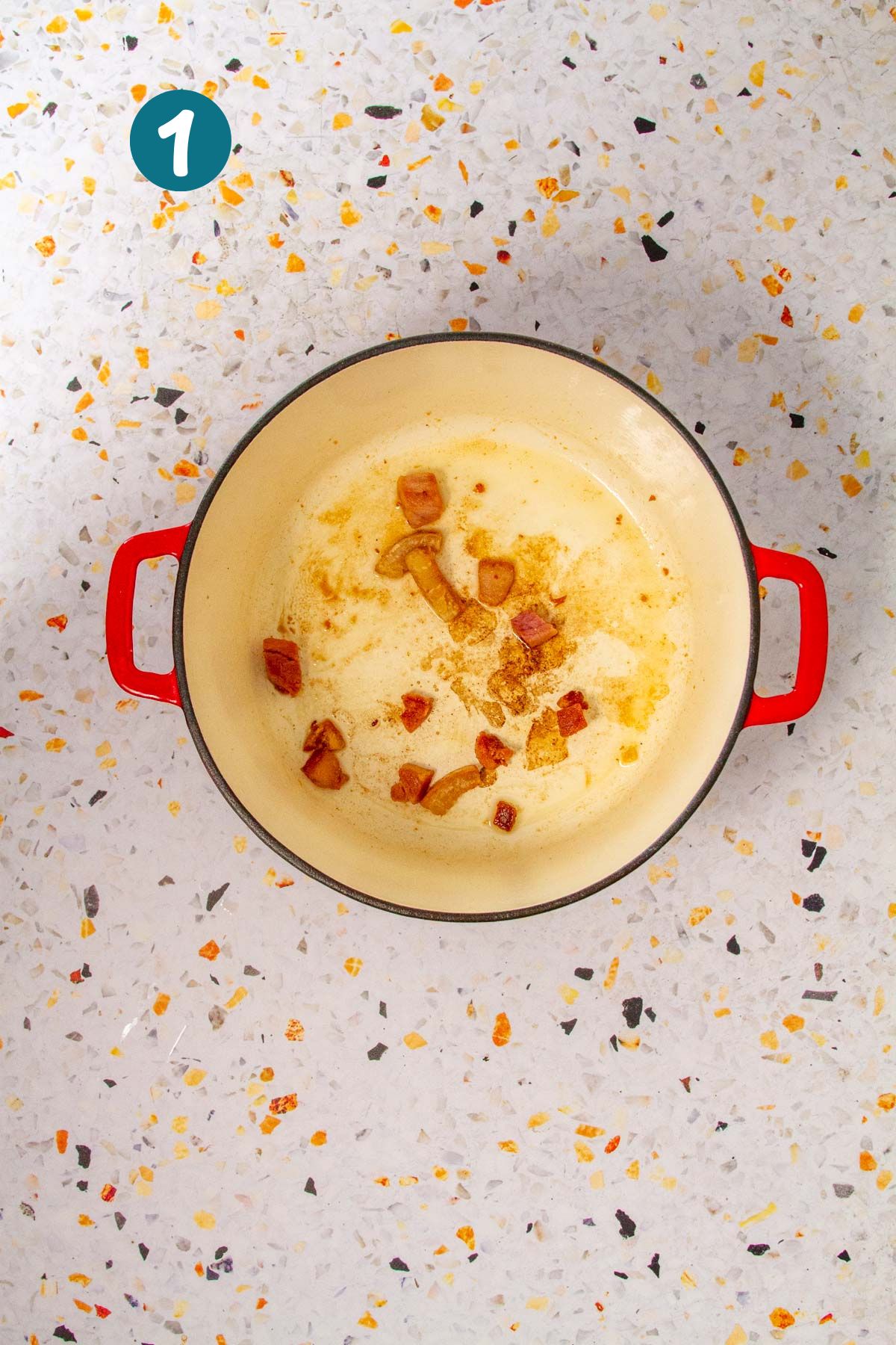 Cubed ham and tocino are browning in a red Dutch oven, the rendered fat creating the flavor base for the rice.