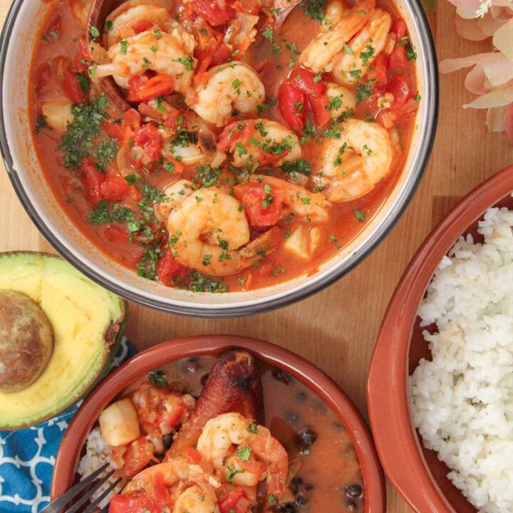 Bowl of Puerto Rican shrimp and scallop stew garnished with parsley, served with white rice and half an avocado on the side.