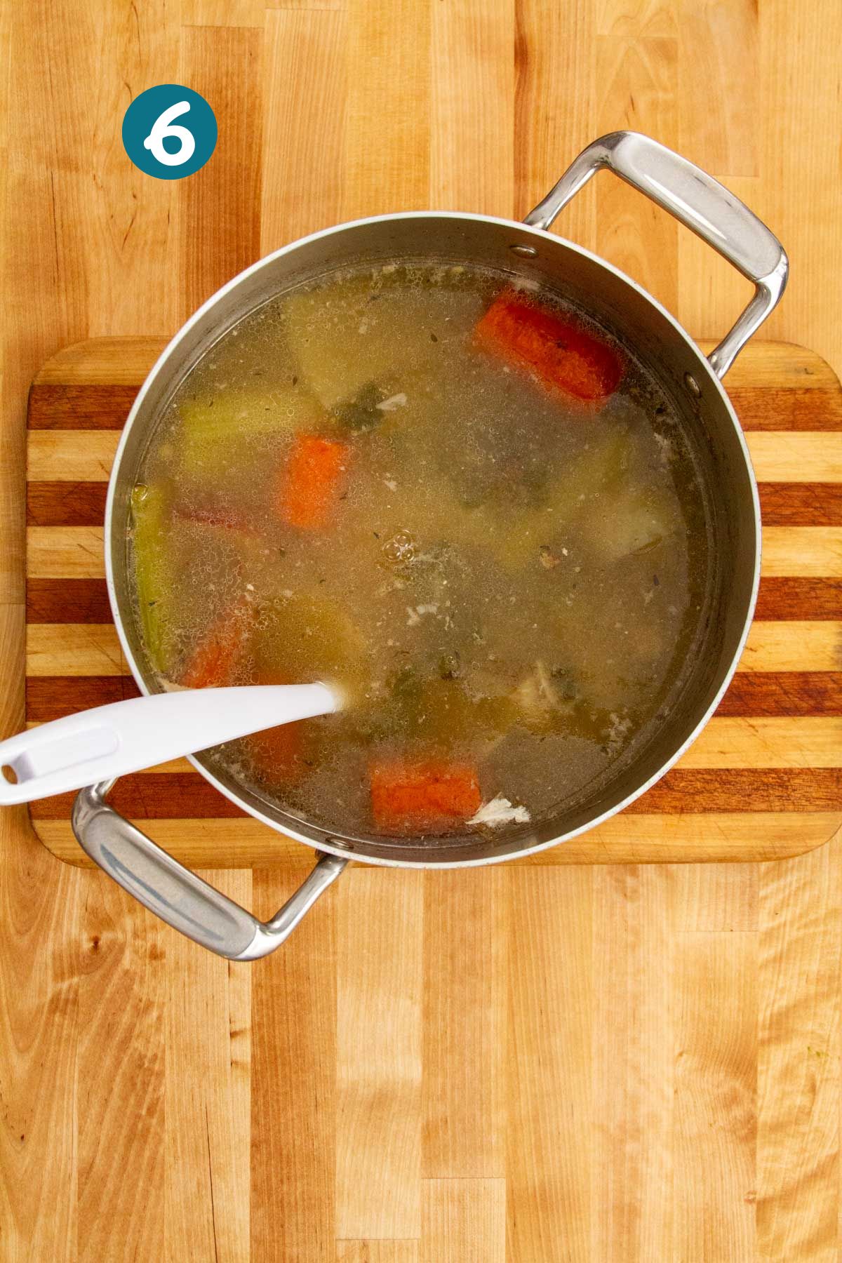 Fish broth simmering with visible vegetables and foam at the surface, ready for skimming.