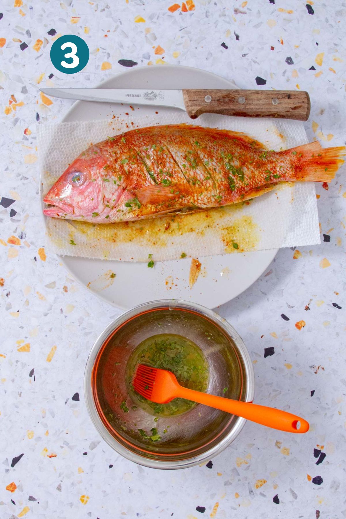 Whole red snapper fully seasoned with sofrito, lemon juice, and spices on a plate.
