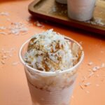 Close-up of a Limber de Coco topped with cinnamon and shredded coconut in a clear plastic cup.