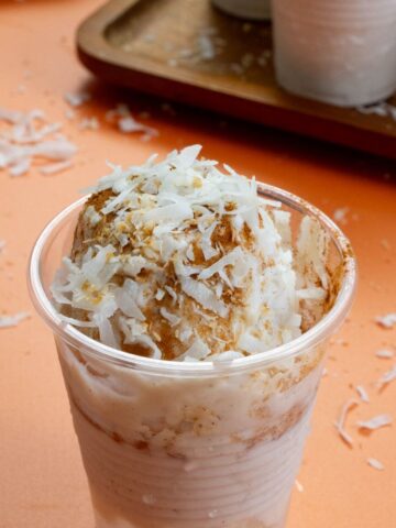 Close-up of a Limber de Coco topped with cinnamon and shredded coconut in a clear plastic cup.