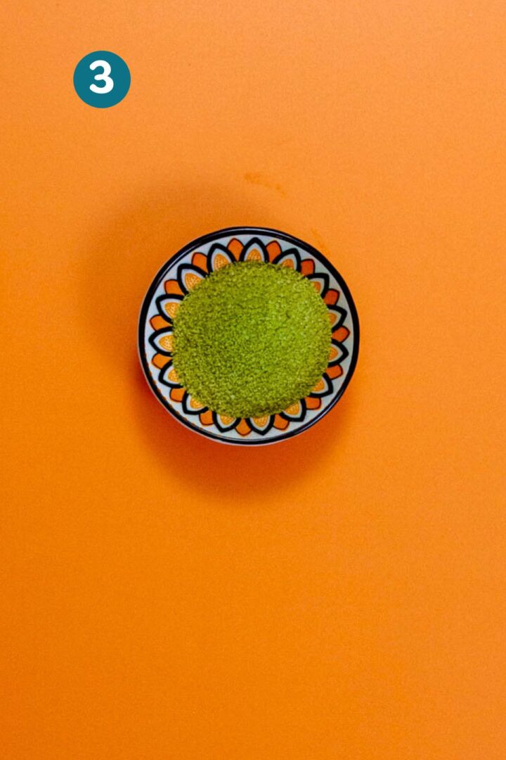 Small bowl of vibrant green matcha powder on an orange background, used for optional color in pistachio limbers.