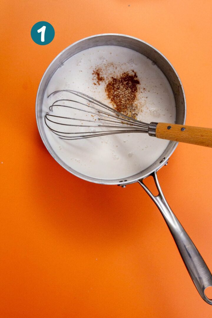 Pot of coconut milk and spices with a whisk, showing the start of the pistachio limber mixture.