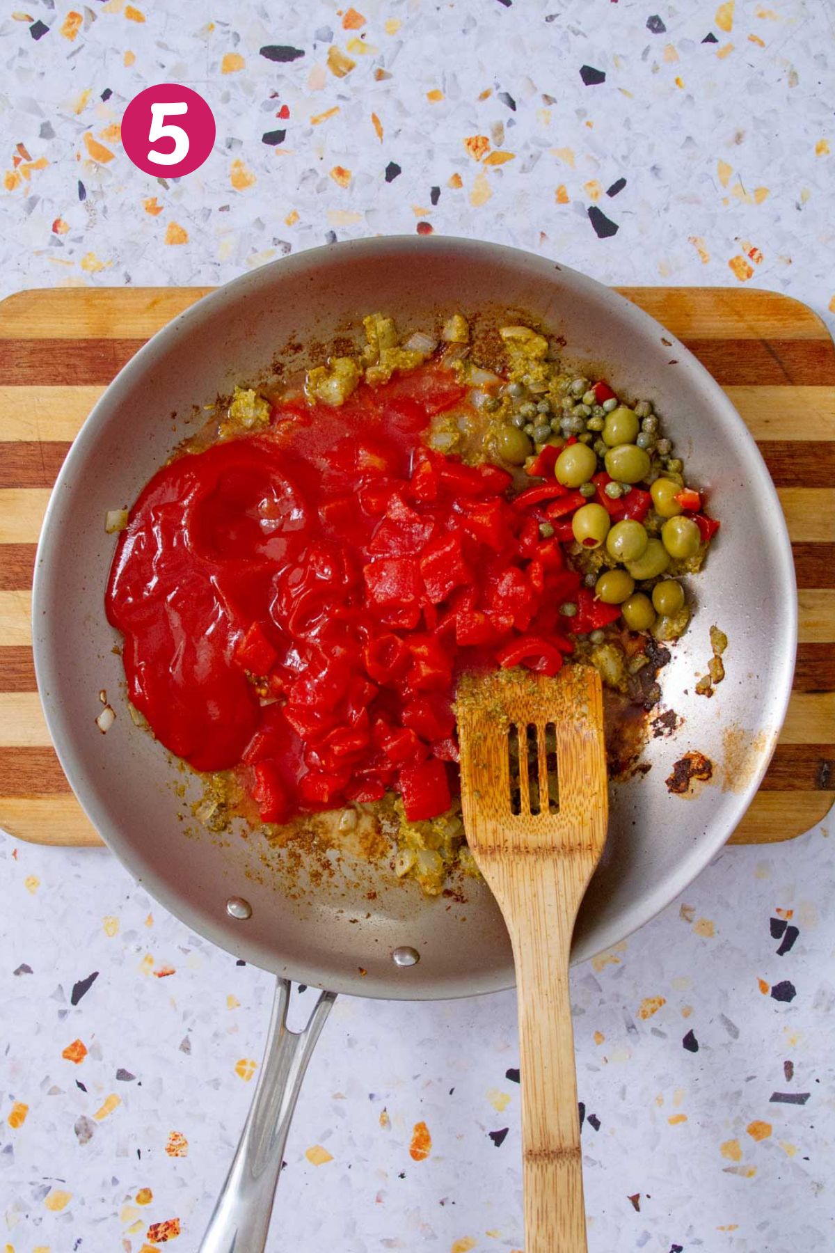 Canned tomatoes, green olives, and capers added to a skillet of sautéed aromatics for Mojo Isleño.