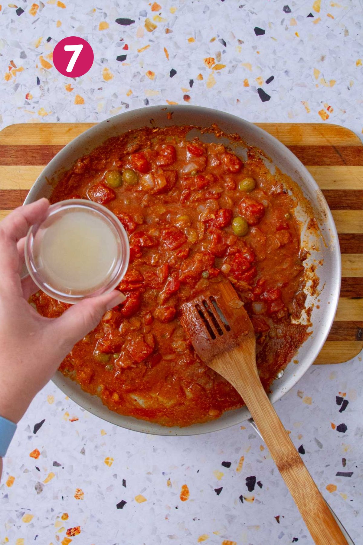 Hand holding a small bowl of lemon juice above a finished skillet of Mojo Isleño sauce.