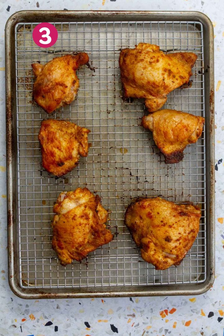 Freshly baked chicken thighs on a wire rack over a baking sheet, golden brown and crispy out of the oven.
