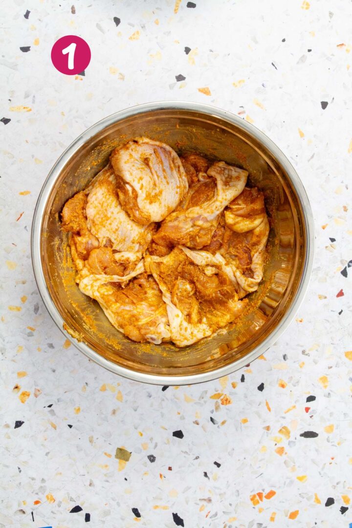 Chicken thighs are fully coated in the seasoning mixture inside a metal bowl, ready to be cooked.