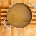 Pot of Puerto Rican fish broth on a wooden cutting board, showing its golden color and clean, simmered appearance.