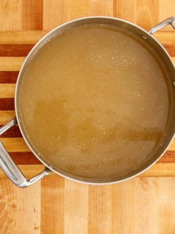 Pot of Puerto Rican fish broth on a wooden cutting board, showing its golden color and clean, simmered appearance.
