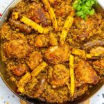 Close-up of Puerto Rican chicken paella with bone-in chicken thighs, longaniza sausage, pigeon peas, and sliced plantains, garnished with fresh cilantro in a large paella pan.