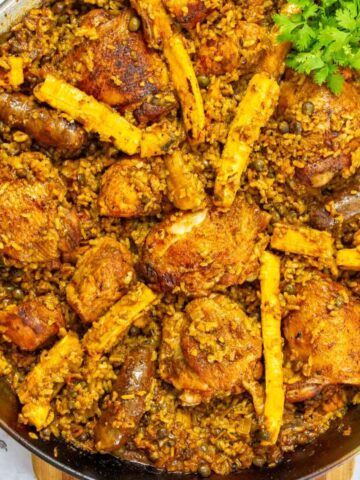 Close-up of Puerto Rican chicken paella with bone-in chicken thighs, longaniza sausage, pigeon peas, and sliced plantains, garnished with fresh cilantro in a large paella pan.