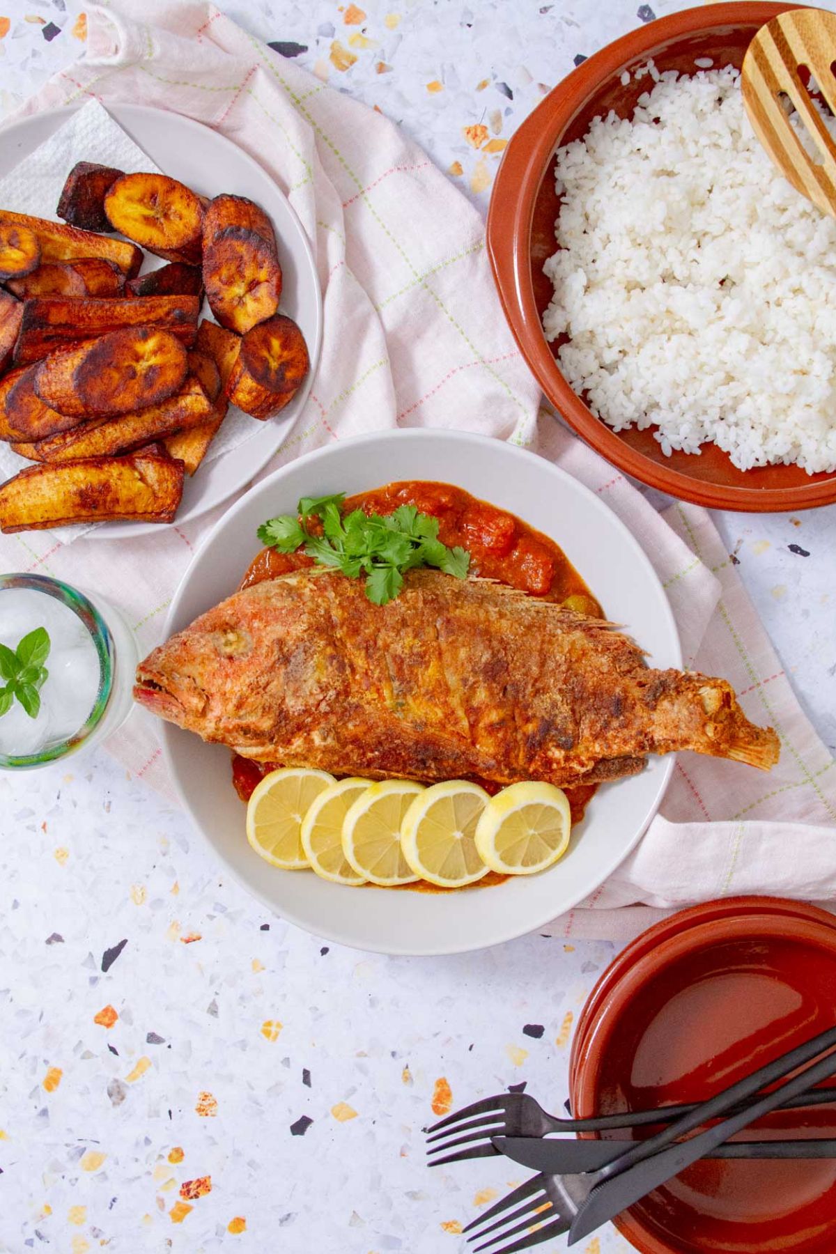 Whole Puerto Rican fried red snapper on tomato sauce with lemon slices, rice, and fried plantains on the side