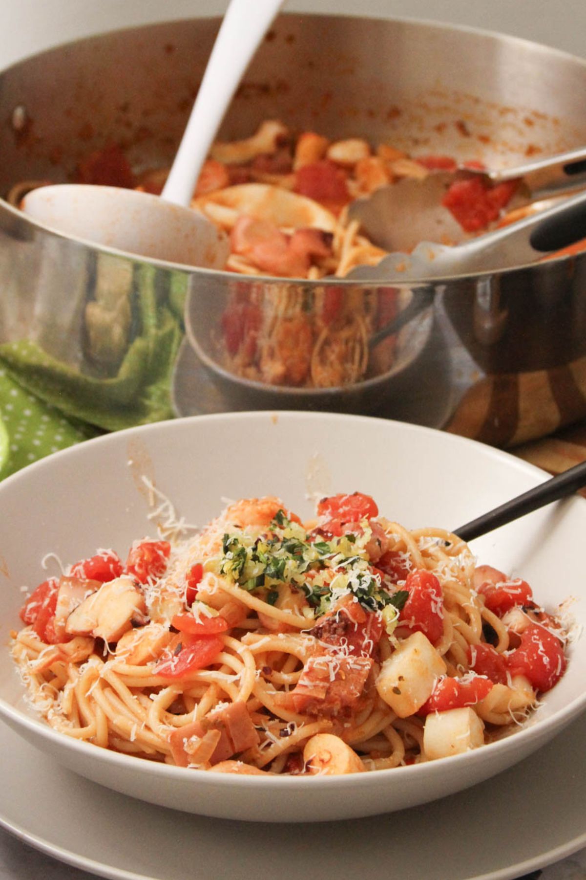 Close-up of seafood pomodoro pasta in a bowl with grated cheese and herb topping, pot in background.