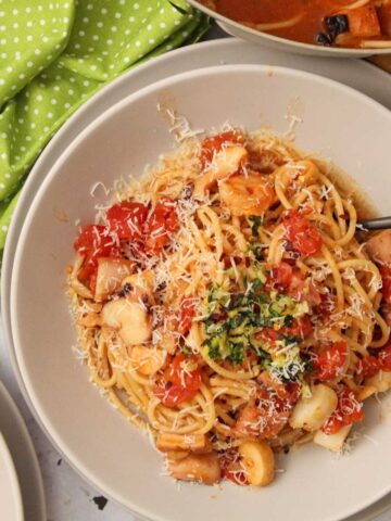 Close-up of Seafood Pomodoro pasta with linguine, topped with culantro gremolata and shredded Parmesan in a white bowl.