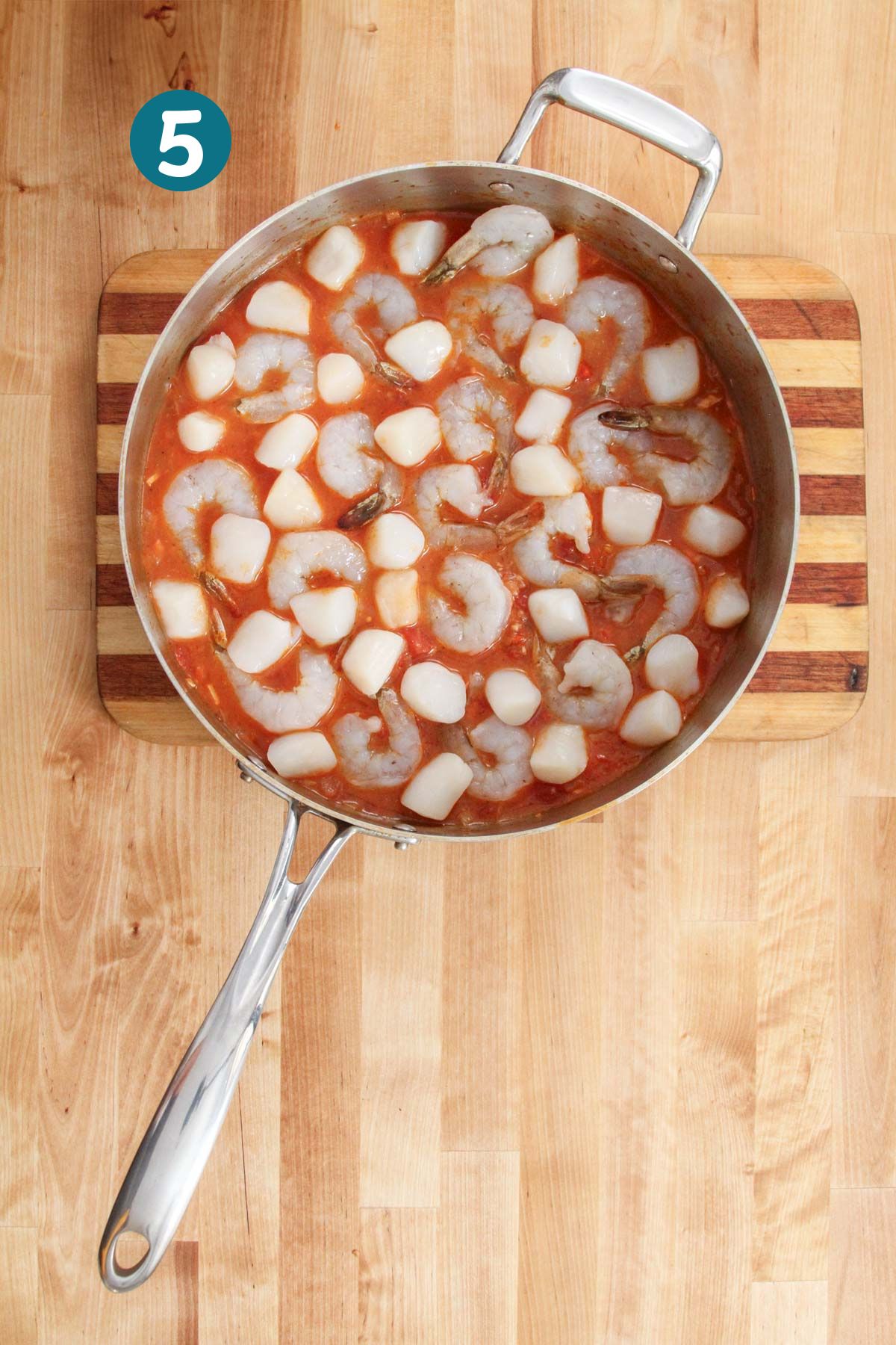 Raw shrimp and scallops are added to the tomato broth in a pan, ready to simmer.