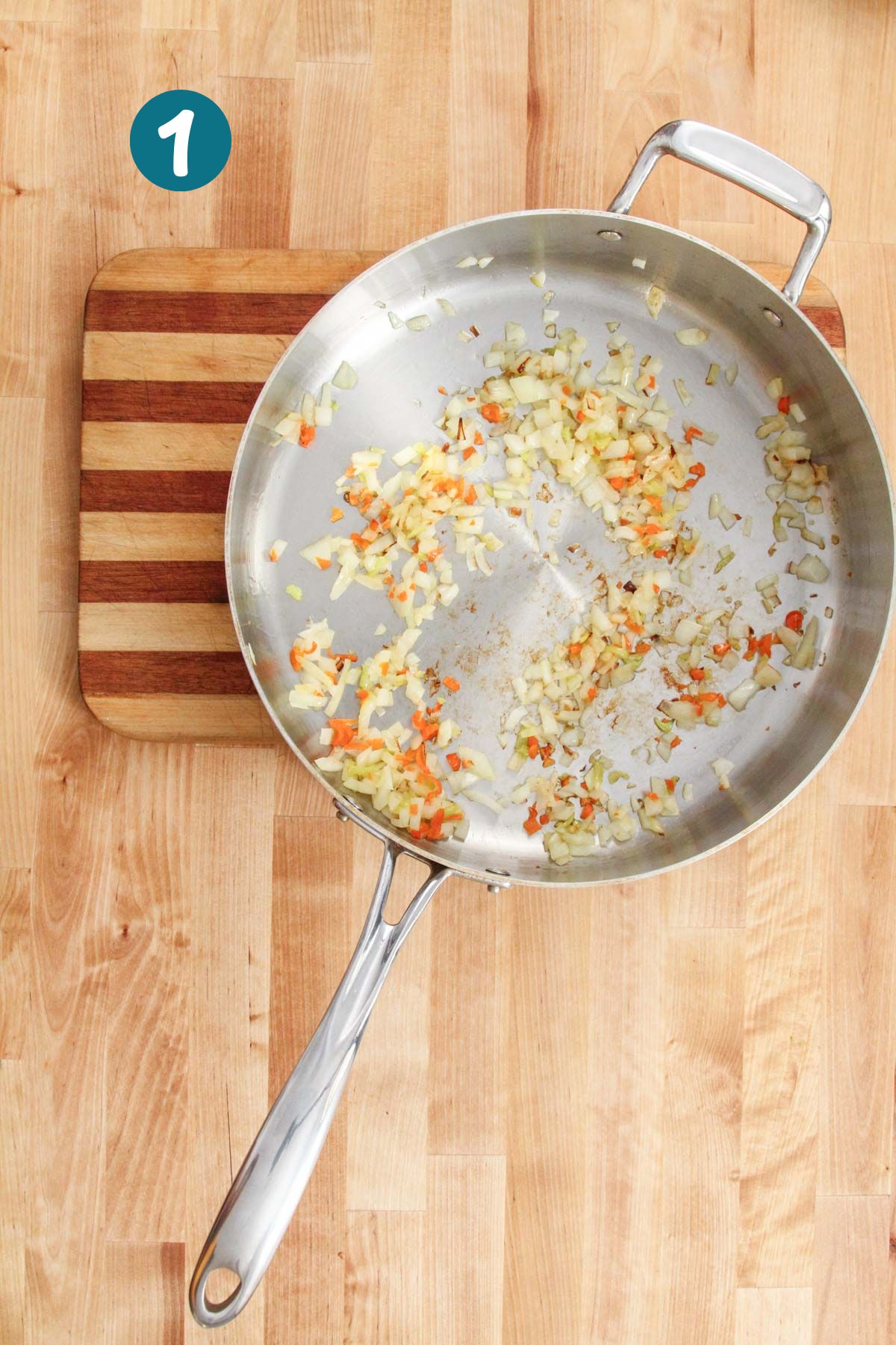 Sautéing chopped onions, garlic, and aji peppers in a stainless steel pan on a wooden cutting board.