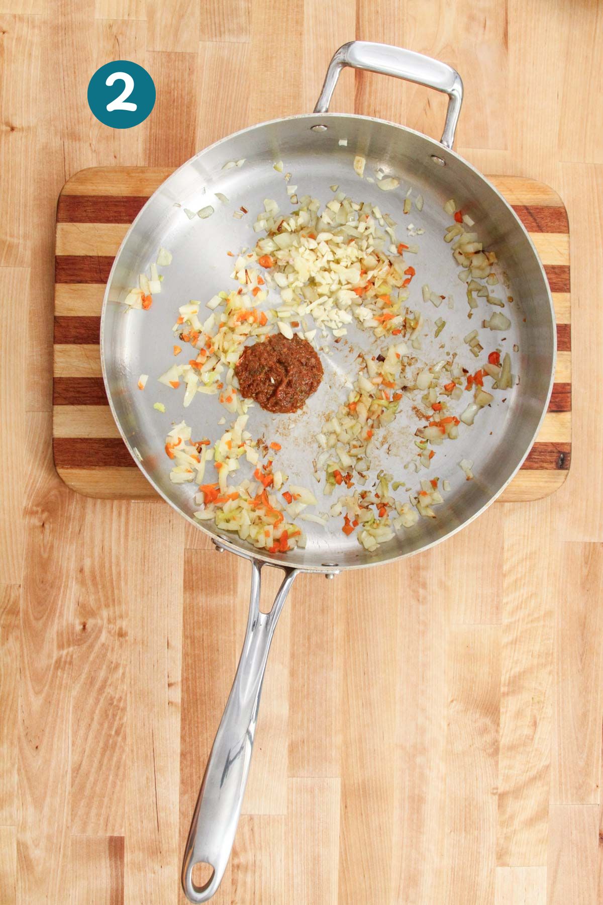 Tomato paste is added to sautéed aromatics in a pan, creating a sofrito base.
