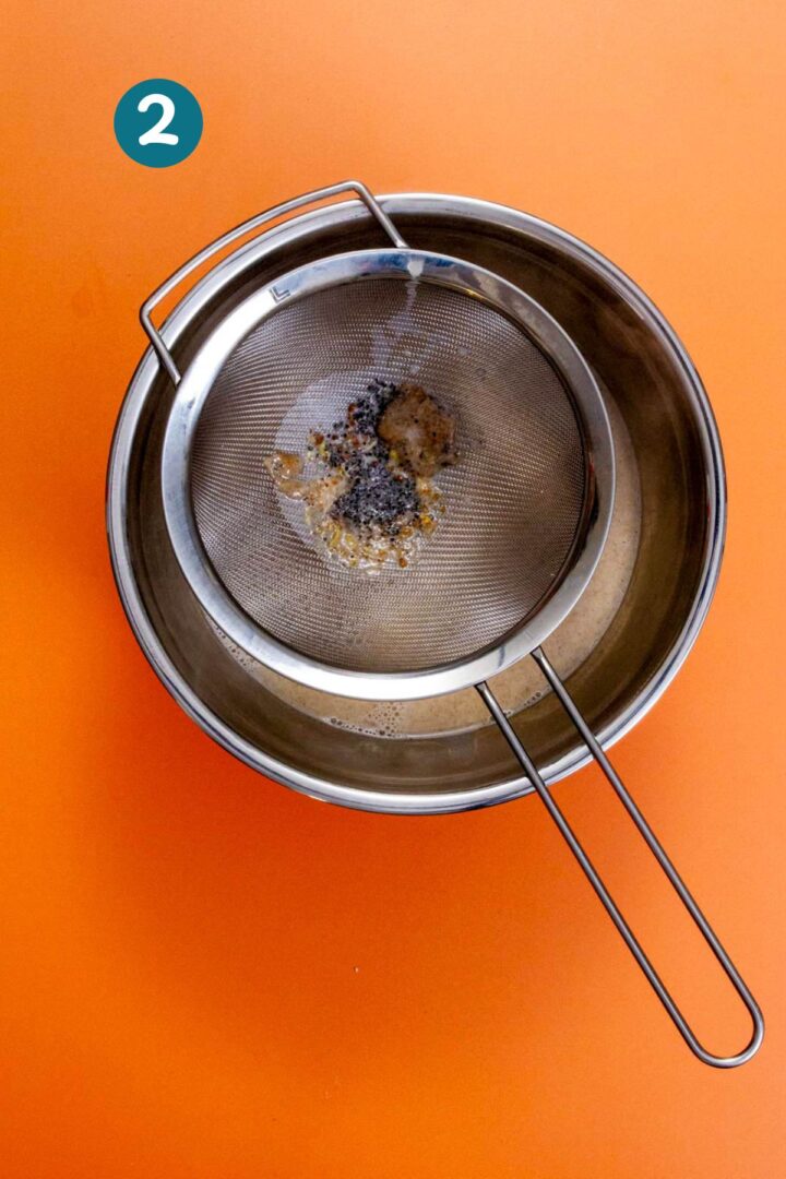 Strainer catching cardamom seeds over a bowl of pistachio limber mixture, to smooth the texture.