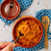 Close-up of a forkful of arroz mamposteao, Puerto Rican rice and beans, held above a bowl on a blue patterned cloth.