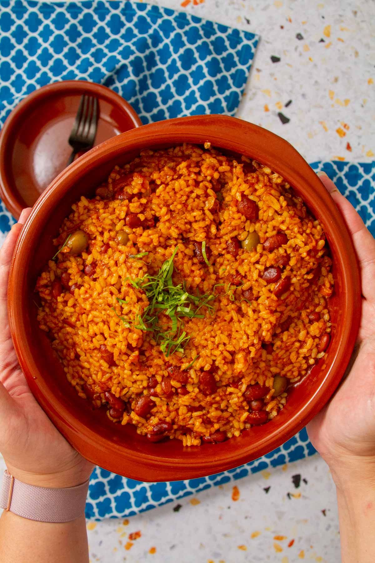 Close-up view of arroz mamposteao in a clay bowl, showing rice, beans, and olives with a garnish of fresh herbs.