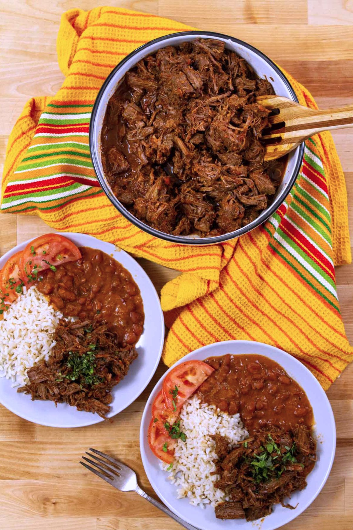 Plated Puerto Rican ropa vieja served with white rice, stewed pink beans, and tomato slices.