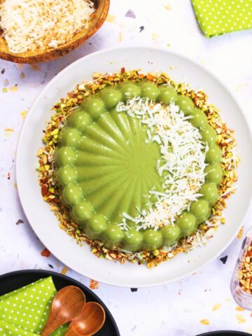 Top view of a molded pistachio tembleque garnished with shredded coconut and chopped pistachios on a white plate.