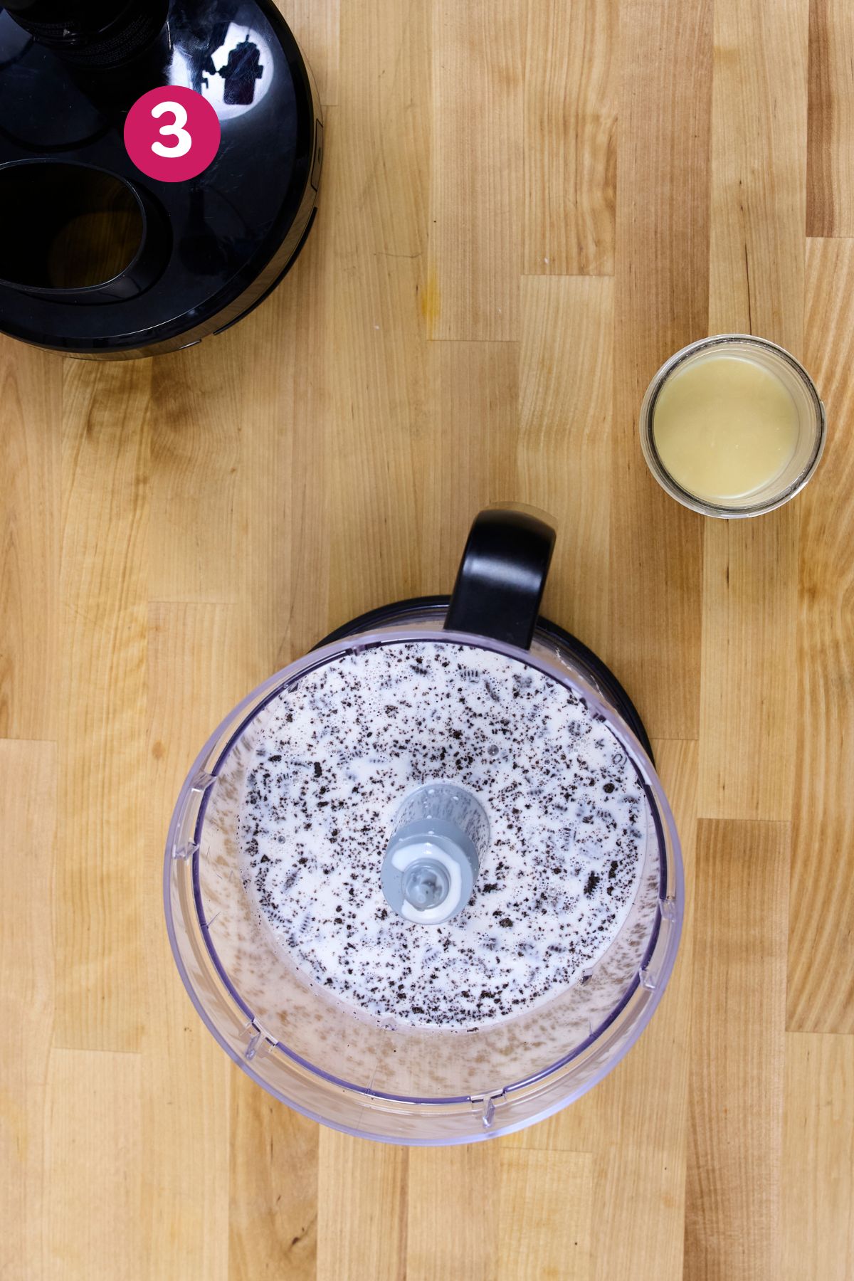 A small jar of condensed milk next to a food processor filled with coconut milk and crushed cookies.