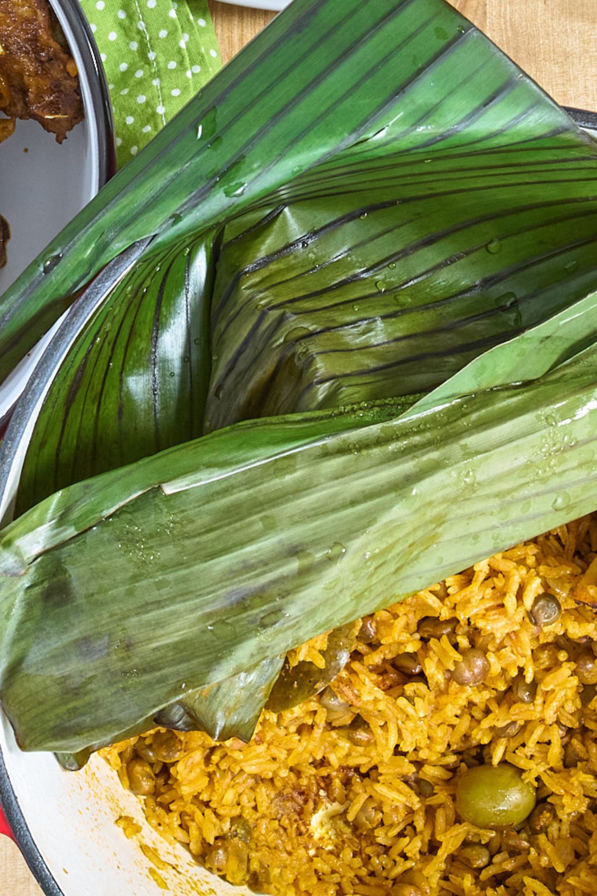 Arroz con gandules covered with banana leaves, served alongside pernil on a holiday table.