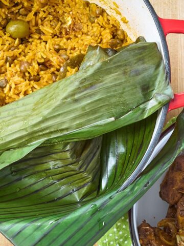 Arroz con gandules covered with banana leaves, served alongside carne frita on a holiday table.
