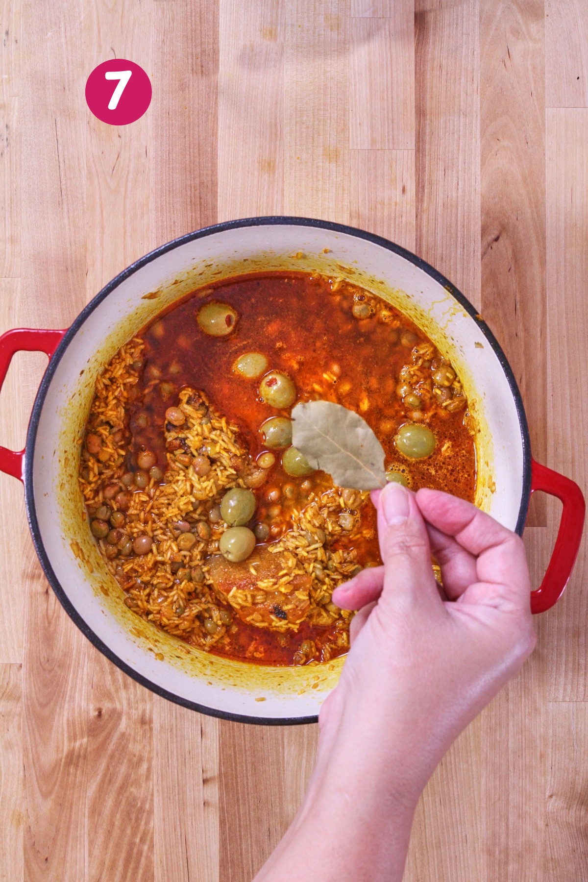 Broth added with olives and bay leaf, beginning the simmering stage of arroz con gandules.