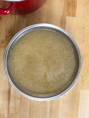 Overhead view of a stainless steel pot filled with chicken broth on a wooden countertop.